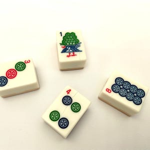 May include: Four ivory-coloured Mahjong tiles with colourful symbols. One tile features a green bird and the number 1. Another shows the number 3 with three circular symbols. The number 4 tile has two sets of circular symbols. The last tile shows the number 8 with eight circular symbols.