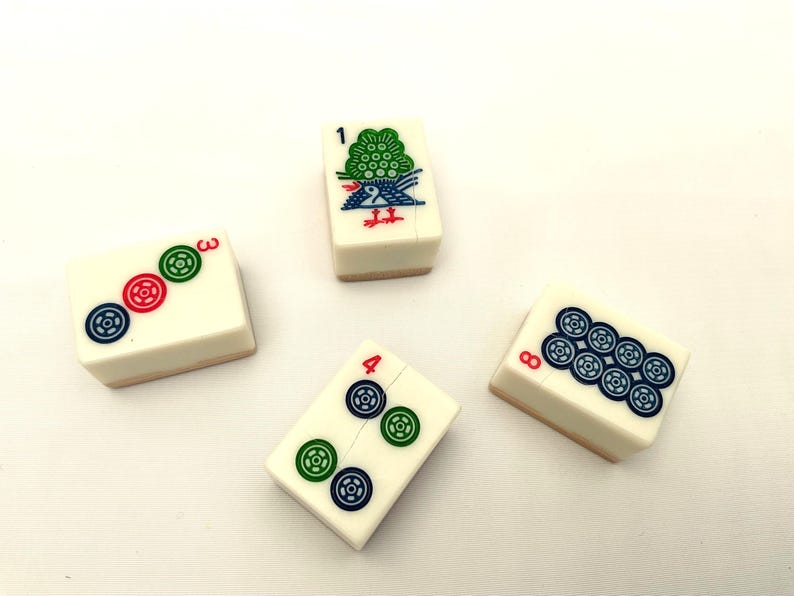 May include: Four ivory-coloured Mahjong tiles with colourful symbols. One tile features a green bird and the number 1. Another shows the number 3 with three circular symbols. The number 4 tile has two sets of circular symbols. The last tile shows the number 8 with eight circular symbols.