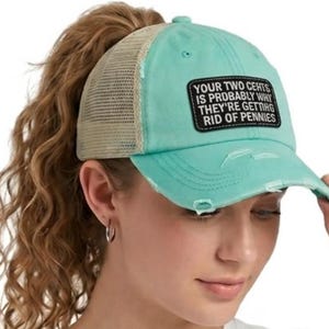 May include: A turquoise baseball cap with a distressed brim and a beige mesh back. A black rectangular patch on the front features the white text: YOUR TWO CENTS IS PROBABLY WHY THEY'RE GETTING RID OF PENNIES. The cap has a high ponytail opening.