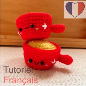 Puede incluir: Artículo de ganchillo rojo de dos piezas con interior amarillo, ojos negros y detalles de cruz blancos. El texto "Tutoriel Français" es visible en la imagen. Un corazón con los colores de la bandera francesa está en el fondo.