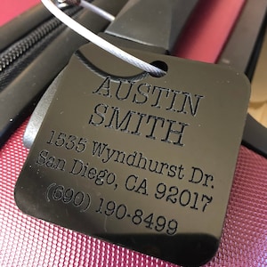 May include: Black luggage tag with white text. The text reads "Austin Smith, 1535 Wyndhurst Dr. San Diego, CA 92017 (690) 190-8499".