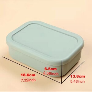 Puede incluir: Una fiambrera rectangular de color verde claro con tapa. La fiambrera mide 18,6 cm de largo, 13,8 cm de ancho y 6,5 cm de alto.