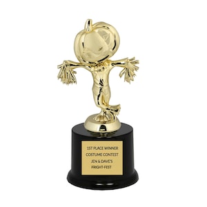 May include: Gold-colored trophy with a pumpkin-headed scarecrow figure. The base is black with a gold plaque that reads "1st Place Winner Costume Contest Jen & Dave's Fright-Fest".