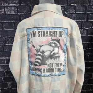 May include: A white and light blue plaid button-up shirt with a graphic on the back that says "I'm Straight Up Not Even Having A Good Time" and features a cartoon raccoon.