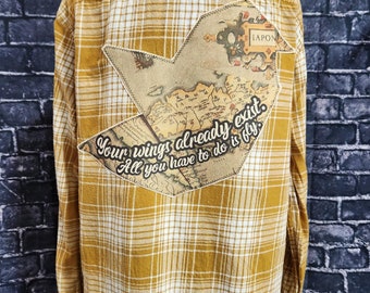 Camisa de franela desgastada con mensaje inspirador y mapa en forma de pájaro: «Tus alas ya existen. Solo tienes que volar». Viajeros, vagabundos.