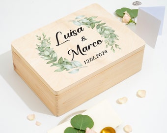 Può includere: Una scatola di legno con una finitura in legno chiaro. Il coperchio presenta un disegno ad acquerello di foglie verdi a forma di corona. Il testo "Luisa & Marco 12.06.2024" è stampato in nero sul coperchio.