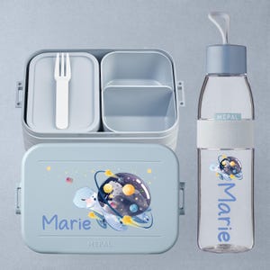 Può includere: Un set di lunch box azzurro con una bottiglia d'acqua abbinata. Il lunch box presenta una tartaruga dei cartoni animati con un design a pianeta e il nome "Marie". La bottiglia d'acqua ha anche il nome "Marie" e una grafica di tartaruga.