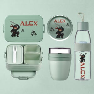 Op de afbeelding: Een set lichtgroene lunchaccessoires, waaronder een lunchbox, een ronde container, een voedselpot en een waterfles. Elk item heeft een ninja-afbeelding en de naam "ALEX" in het rood.