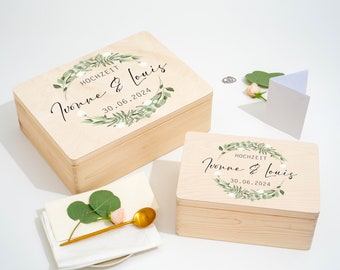 Può includere: Due scatole di legno con coperchi, decorate con una ghirlanda di fiori e il testo "Hochzeit Yvonne & Louis 30.06.2024".