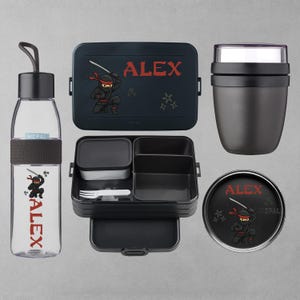 Könnte beinhalten: Ein Set aus schwarzen und transparenten Lunch-Accessoires mit Ninja-Motiv. Enthält eine Wasserflasche, eine Lunchbox, einen Behälter und einen runden Behälter, alle mit dem Namen "ALEX" und einer Ninja-Grafik.