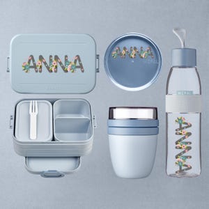 Op de afbeelding: Een lichtblauwe lunchset met de naam "ANNA" in bloemrijke letters. De set bevat een lunchbox, een ronde container, een voedselpot en een waterfles. De lunchbox heeft een vork en compartimenten.