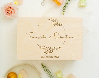 Puede incluir: Una caja de madera con un diseño de corona floral y el texto "Franziska & Sebastian" y "26. Februar 2020" grabado en la tapa.