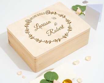 Puede incluir: Una caja de madera con tapa, grabada con una corona de flores, la fecha "18.05.2022" y los nombres "Larissa & Robert".
