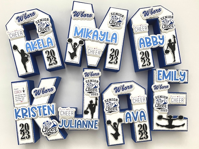 May include: A set of six blue and white foam letters spelling out the word "KELSEY" decorated with cheerleading-themed embellishments. Each letter has a white background with blue trim and features a cheerleader silhouette, the words "Senior Cheer", and the year "2023". The letters are decorated with glitter and other embellishments.