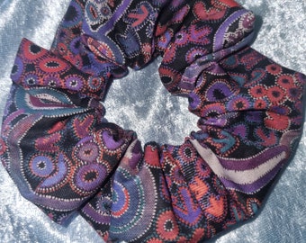 May include: A black scrunchie with a paisley pattern in shades of purple, pink, and teal.