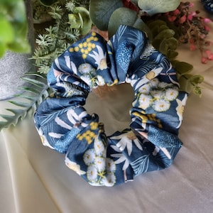May include: A blue and white floral patterned scrunchie with yellow accents. The scrunchie is made of fabric and is designed to hold hair in place.