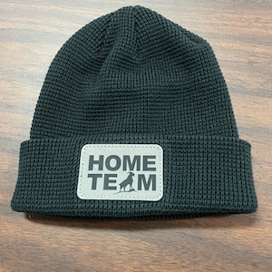 May include: Black knitted beanie with a grey patch that says "HOME TEAM" with a silhouette of a mountain goat.