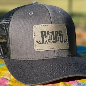 May include: A grey and black trucker hat with a brown leather patch that says "RUFFS" in a stylised font.