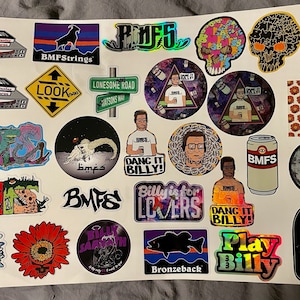 May include: A collection of colorful stickers featuring various designs, including a skull, a fish, a sunflower, and a cartoon character. The stickers have text that reads "BMFS", "Dang It Billy!" and "Play Billy".