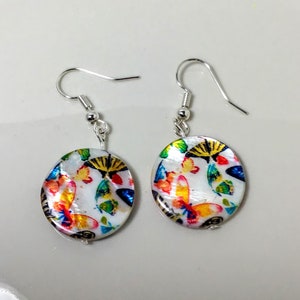 Puede incluir: Un par de pendientes de plata con colgantes redondos, blancos, iridiscentes, de nácar con un diseño de mariposa colorido.