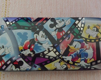 May include: A rectangular tin box with a colorful design featuring Mickey Mouse, Donald Duck, and Goofy. The characters are surrounded by film strips.
