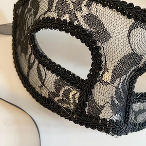 May include: Black lace masquerade mask with a black trim around the edges. The mask has a delicate floral pattern.