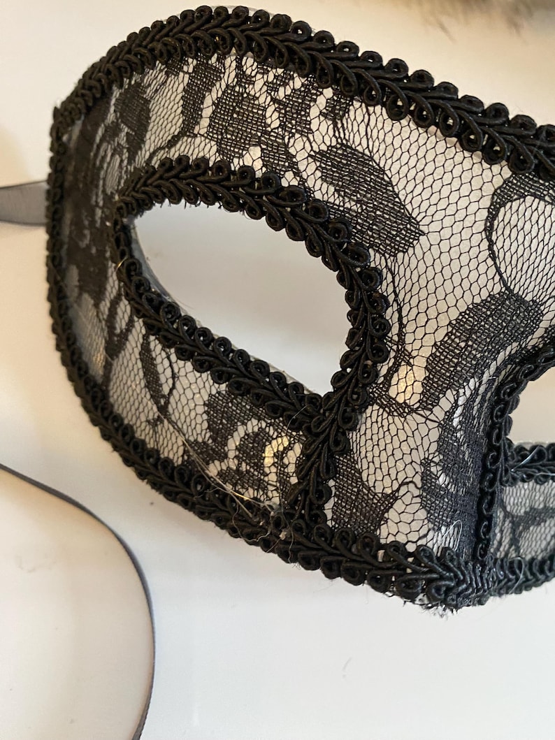 May include: Black lace masquerade mask with a black trim around the edges. The mask has a delicate floral pattern.