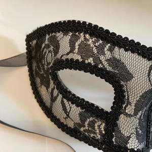 May include: A black lace eye mask with a black trim. The mask has a delicate floral pattern.