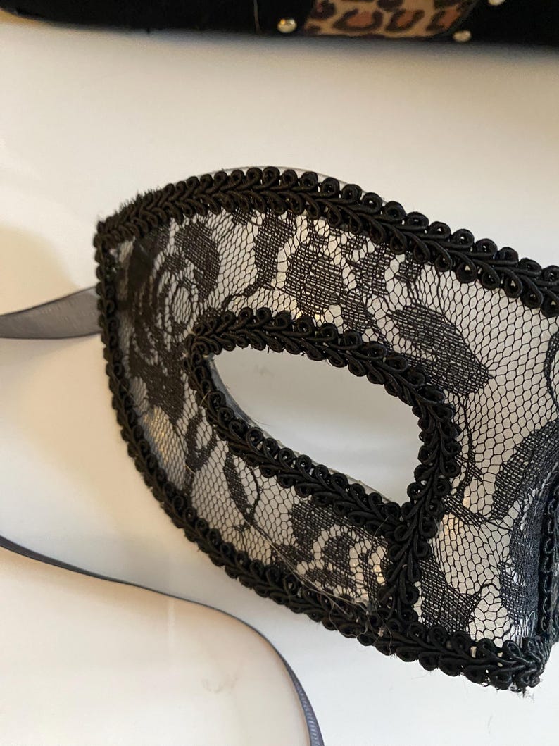 May include: A black lace eye mask with a black trim. The mask has a delicate floral pattern.