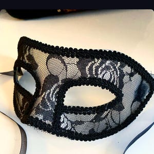 May include: A black lace masquerade mask with a black ribbon. The mask has a delicate floral pattern and is trimmed with a black satin ribbon.