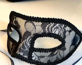 May include: A black lace masquerade mask with a black ribbon. The mask has a delicate floral pattern and is trimmed with a black satin ribbon.