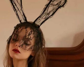 Puede incluir: Una diadema de orejas de conejo de encaje negro con una máscara para los ojos a juego. La diadema la lleva una persona con el pelo largo y castaño.