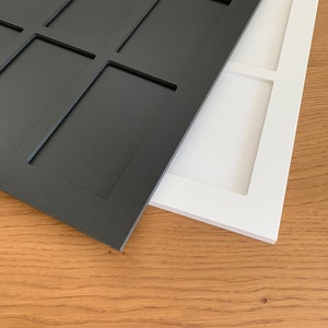 Puede incluir: Dos bandejas rectangulares de madera, una negra y otra blanca, con compartimentos empotrados. Las bandejas est&aacute;n colocadas en &aacute;ngulo, mostrando su dise&ntilde;o y colores contrastantes. El fondo es una superficie de madera marr&oacute;n claro.