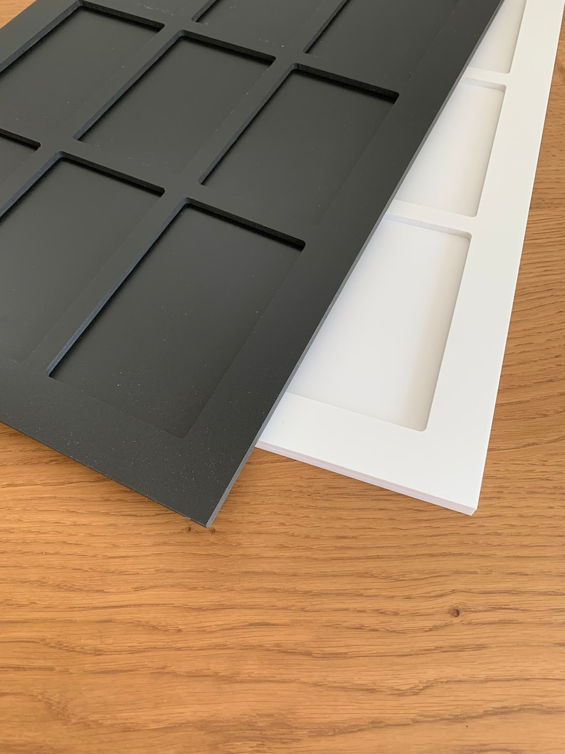 Puede incluir: Dos bandejas rectangulares de madera, una negra y otra blanca, con compartimentos empotrados. Las bandejas est&aacute;n colocadas en &aacute;ngulo, mostrando su dise&ntilde;o y colores contrastantes. El fondo es una superficie de madera marr&oacute;n claro.