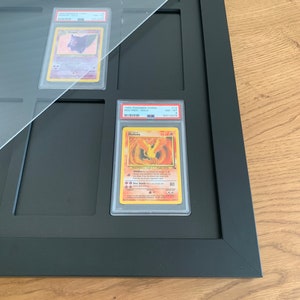 Puede incluir: Un marco negro con una parte superior de acr&iacute;lico transparente contiene una carta Pok&eacute;mon clasificada. La carta es un Moltres del set Fossil, clasificada NM-MT por PSA con una calificaci&oacute;n de 8. El n&uacute;mero de la carta es 113 y el n&uacute;mero de PSA es 54712276.