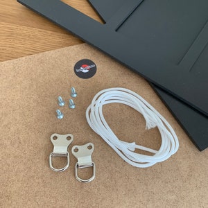 Puede incluir: Un marco de fotos negro con m&uacute;ltiples aberturas, un tablero trasero marr&oacute;n claro y herrajes. Los herrajes incluyen tornillos, dos anillas en D met&aacute;licas y un cord&oacute;n blanco para colgar. Tambi&eacute;n se incluye una pegatina con el texto "Long Lost Gems".