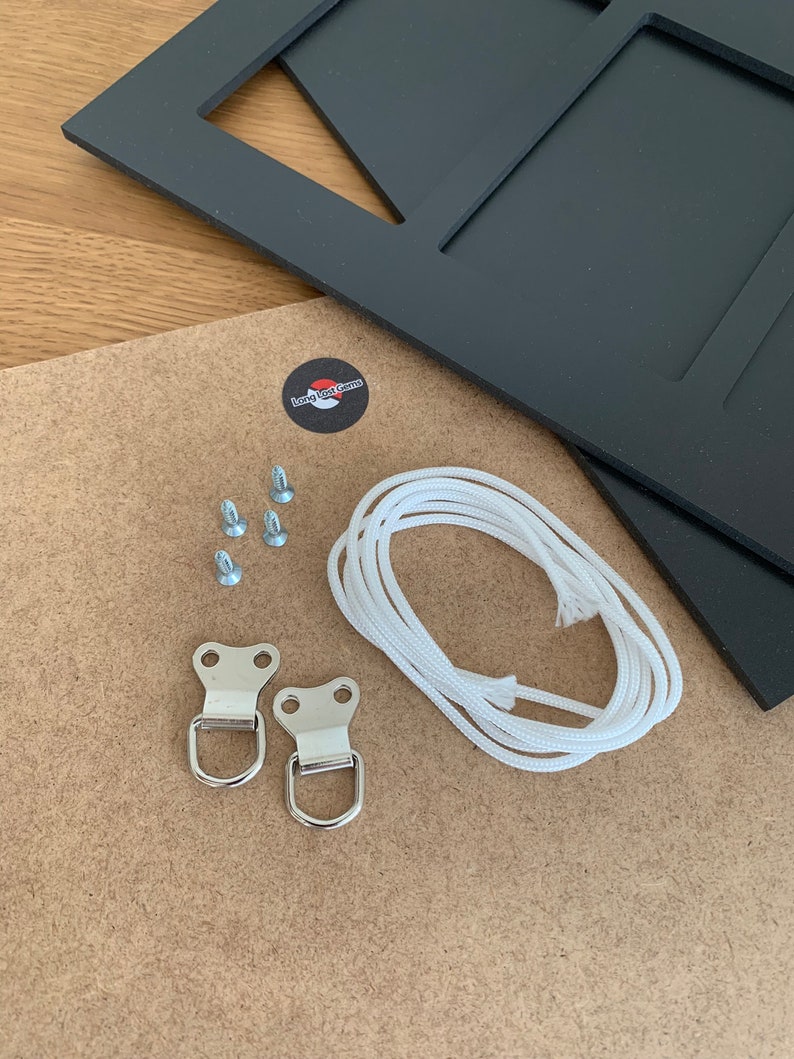 Puede incluir: Un marco de fotos negro con m&uacute;ltiples aberturas, un tablero trasero marr&oacute;n claro y herrajes. Los herrajes incluyen tornillos, dos anillas en D met&aacute;licas y un cord&oacute;n blanco para colgar. Tambi&eacute;n se incluye una pegatina con el texto "Long Lost Gems".