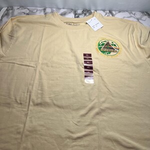May include: Tan XL t-shirt with a circular graphic featuring a pyramid, waves, and the text "Pink Floyd" and "Dark Side of the Moon". The shirt has a crew neck and a size tag.