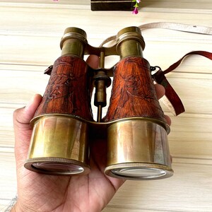 K&ouml;nnte beinhalten: Vintage-Fernglas aus Messing mit Lederbezug und aufwendigen Holzschnitzereien. Das Fernglas hat einen Trageriemen.