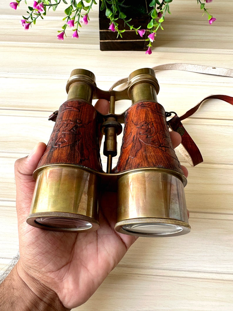 K&ouml;nnte beinhalten: Vintage-Fernglas aus Messing mit Lederbezug und aufwendigen Holzschnitzereien. Das Fernglas hat einen Trageriemen.