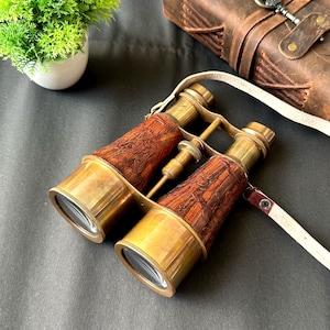 K&ouml;nnte beinhalten: Messing-Fernglas mit einem gravierten Holzkasten und einem wei&szlig;en Lederriemen. Das Fernglas hat ein Vintage-Look und -Gef&uuml;hl.