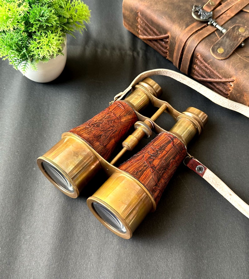 K&ouml;nnte beinhalten: Messing-Fernglas mit einem gravierten Holzkasten und einem wei&szlig;en Lederriemen. Das Fernglas hat ein Vintage-Look und -Gef&uuml;hl.