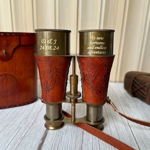 K&ouml;nnte beinhalten: Messing-Fernglas mit Lederetui und -band. Das Fernglas hat ein Blumenmuster und ist mit dem Text "To new horizons and endless adventures" graviert.