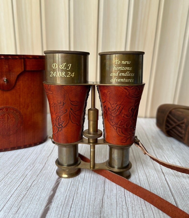 K&ouml;nnte beinhalten: Messing-Fernglas mit Lederetui und -band. Das Fernglas hat ein Blumenmuster und ist mit dem Text "To new horizons and endless adventures" graviert.