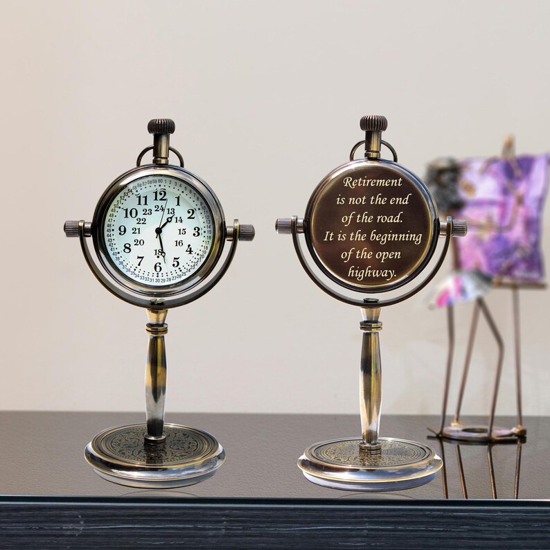 Puede incluir: Un reloj de escritorio de estilo vintage con esfera redonda y soporte. La esfera muestra la hora con n&uacute;meros negros sobre fondo blanco. El segundo reloj tiene el texto: "La jubilaci&oacute;n no es el final del camino. Es el comienzo de la autopista abierta."