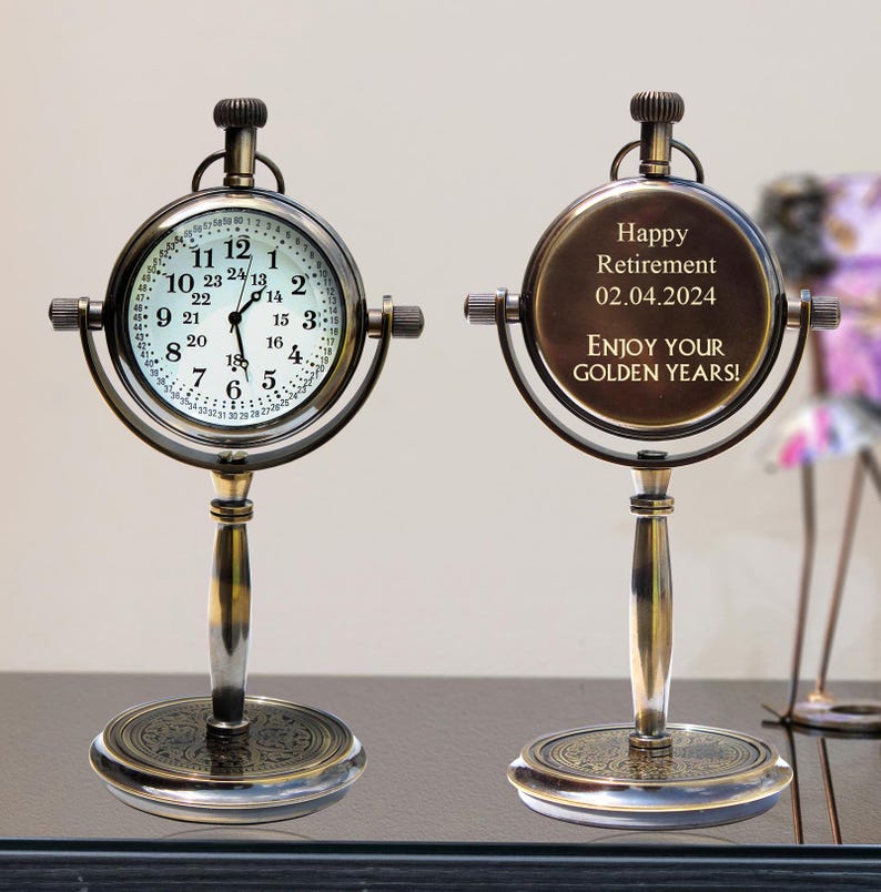 Puede incluir: Un reloj de escritorio de estilo vintage con esfera redonda y base decorativa. La esfera muestra la hora, mientras que la parte trasera del reloj tiene el texto "Happy Retirement 02.04.2024 ENJOY YOUR GOLDEN YEARS!" en tono dorado.