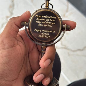 Puede incluir: Un reloj de escritorio de lat&oacute;n de estilo vintage con dise&ntilde;o de br&uacute;jula. La esfera del reloj presenta el texto grabado: "Never underestimate different you have made and lives you have touched. Happy retirement !!! ~Gayan 30.08.2024."