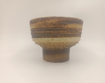Pode incluir: Um vaso de cerâmica marrom e branco com uma parte superior larga e redonda e uma base estreita. O vaso tem um design texturizado e em camadas.