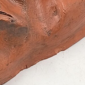 Pode incluir: Close-up de uma escultura de terracota de um rosto. A escultura est&aacute; inacabada e mostra a textura do barro.