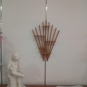 May include: A white statue of a child reading a book, a wooden wall decor, and a decorative plate. The wall decor is made of thin wooden slats arranged in a fan shape. The plate has a rectangular shape with a striped design.
